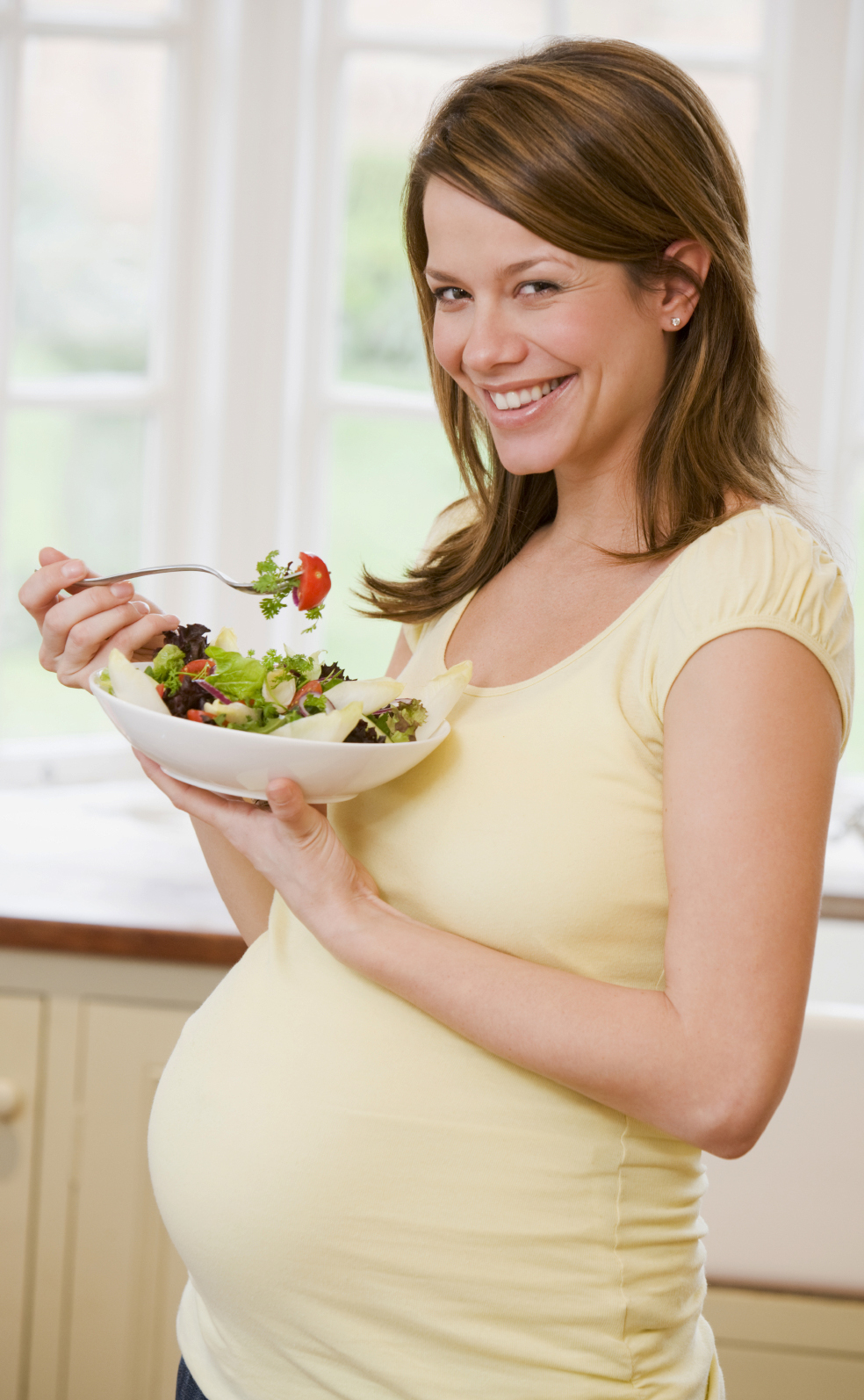 Pregnant woman in kitchen eating a salad smiling
